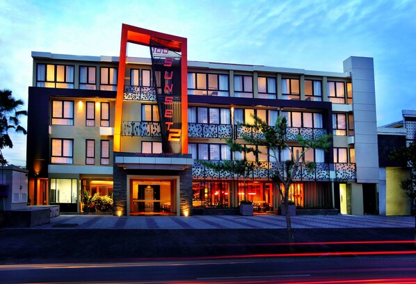 Un hotel moderno con un llamativo letrero vertical, varios balcones y una entrada bien iluminada.