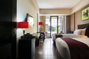 Habitación de hotel con dos camas, un escritorio, una silla y un balcón con cortinas.