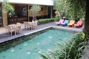 Zona de piscina con sillones reclinables, un bar y un área de estar con mesas y sillas.