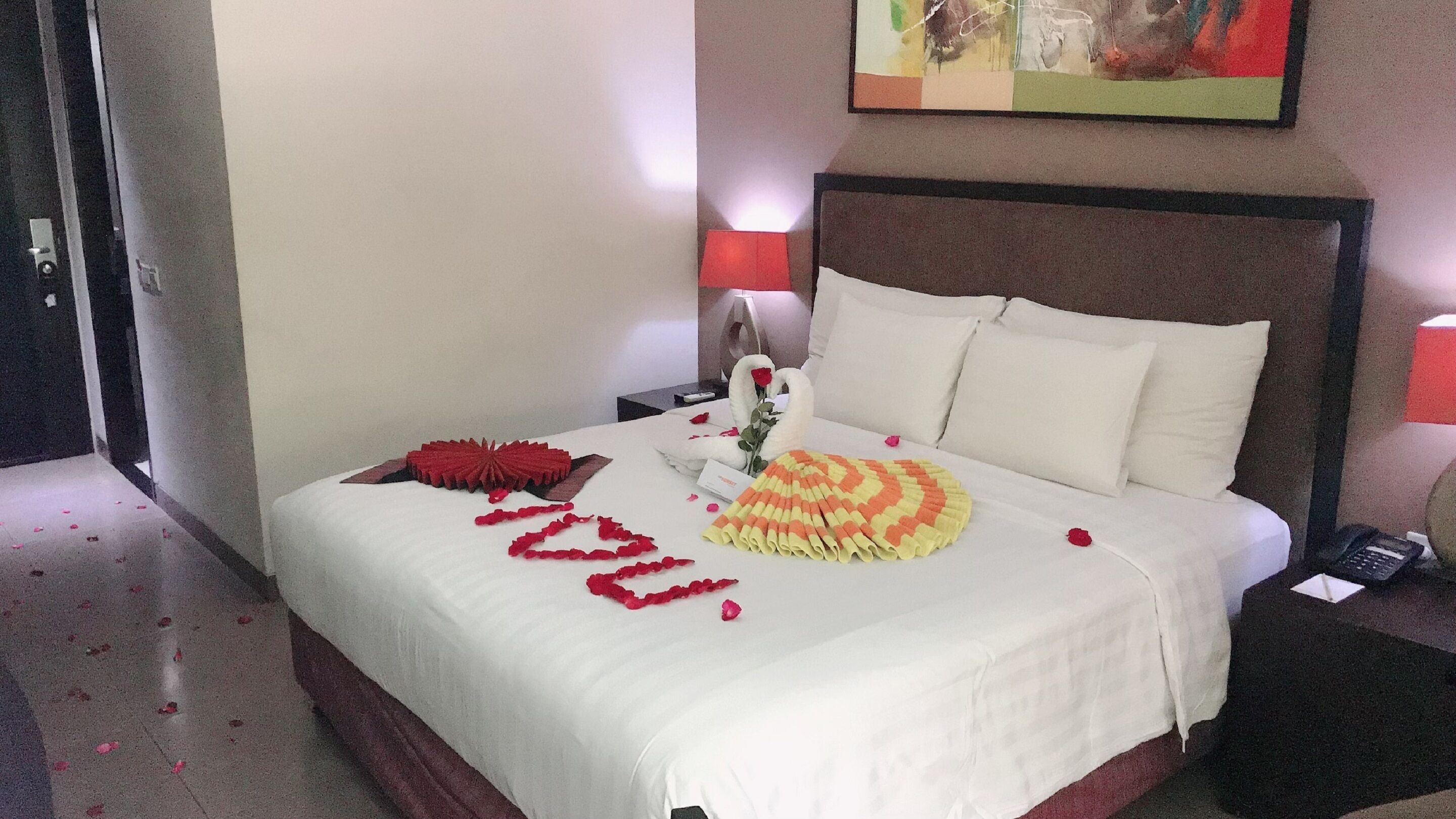 A hotel room with a neatly made bed, a bedside table with a lamp, and a painting on the wall.