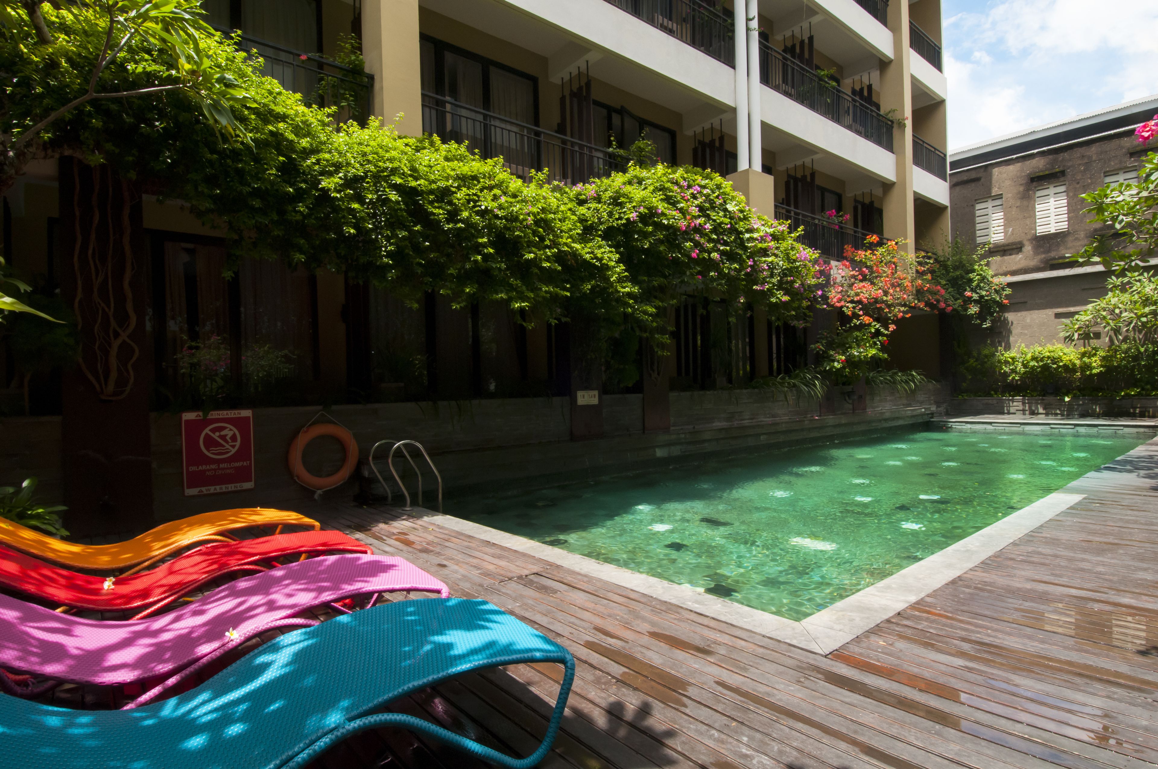 A swimming pool with clear water, surrounded by a wooden deck and lush greenery.