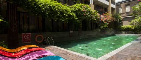 A swimming pool with clear water, surrounded by a wooden deck and lush greenery.