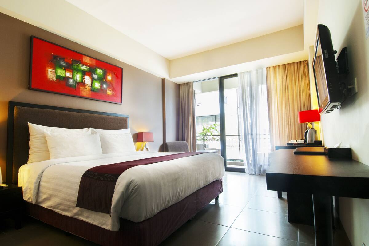 Une chambre d’hôtel avec un lit, un bureau, une télévision et une fenêtre avec des rideaux.