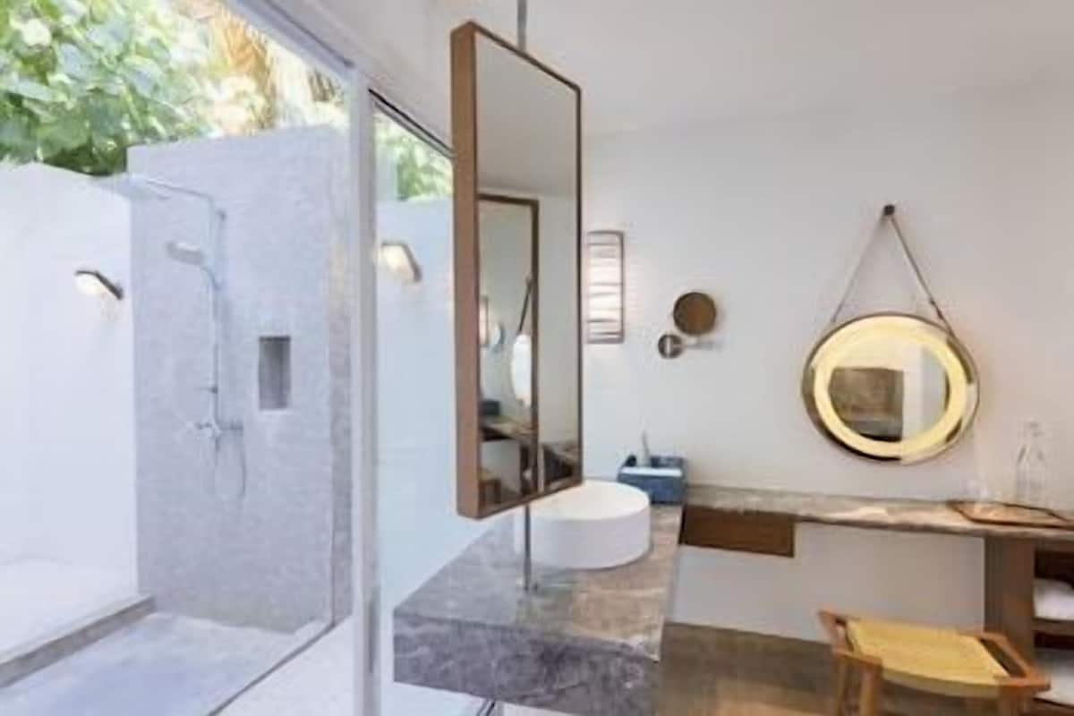 Een moderne badkamer met een douche met glazen wand, een marmeren wastafel en een ronde spiegel.