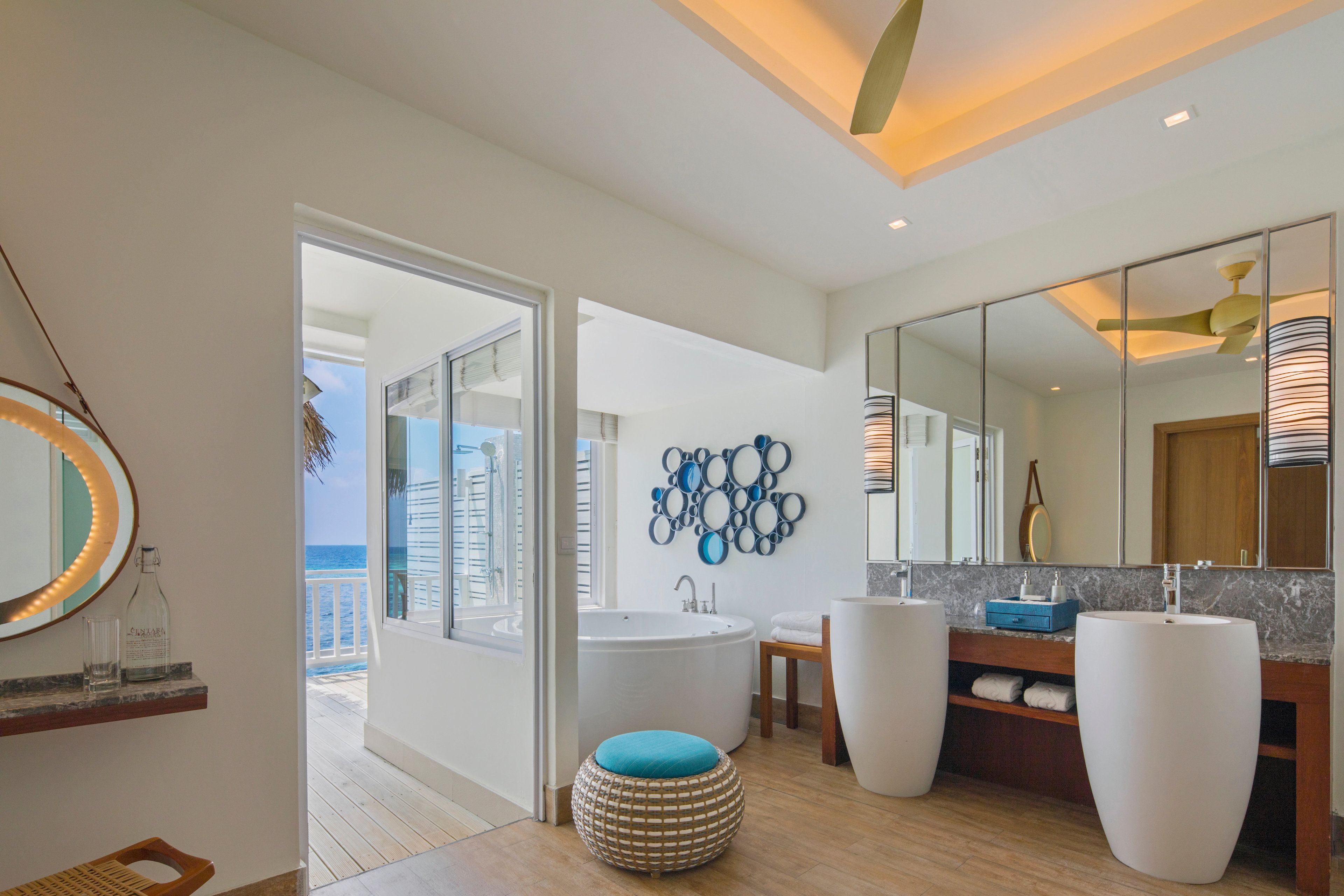 A modern bathroom with a large bathtub, two sinks, a mirror, and a decorative wall piece.