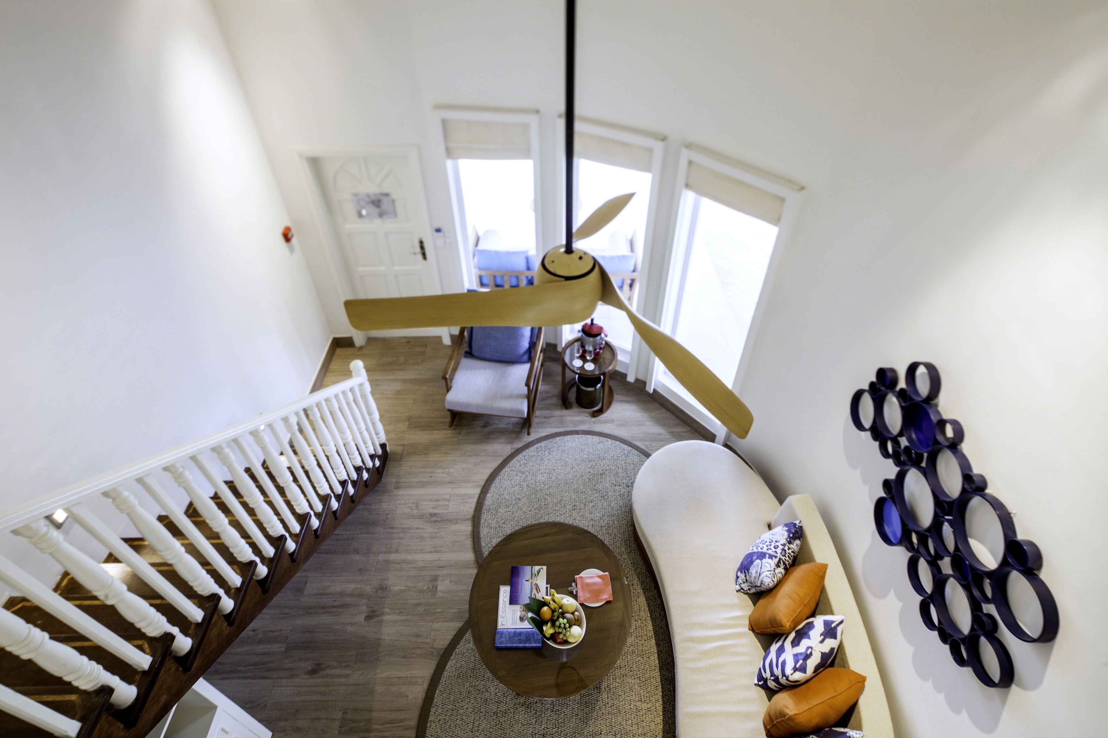 A spacious living area with a high ceiling, a wooden staircase, a large window, and a modern light fixture.