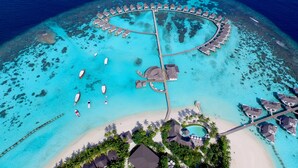 An aerial view of a resort with overwater bungalows arranged in a circular pattern around a central pool, connected by walkways.