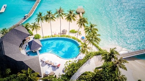 An aerial view of a resort with overwater bungalows, a swimming pool, and a beach area.