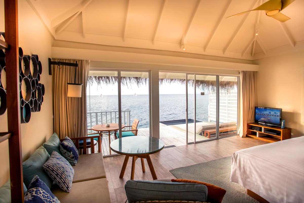 Een kamer met een bed, een televisie, een glazen tafel, een bank en uitzicht op de zee door grote schuifdeuren.