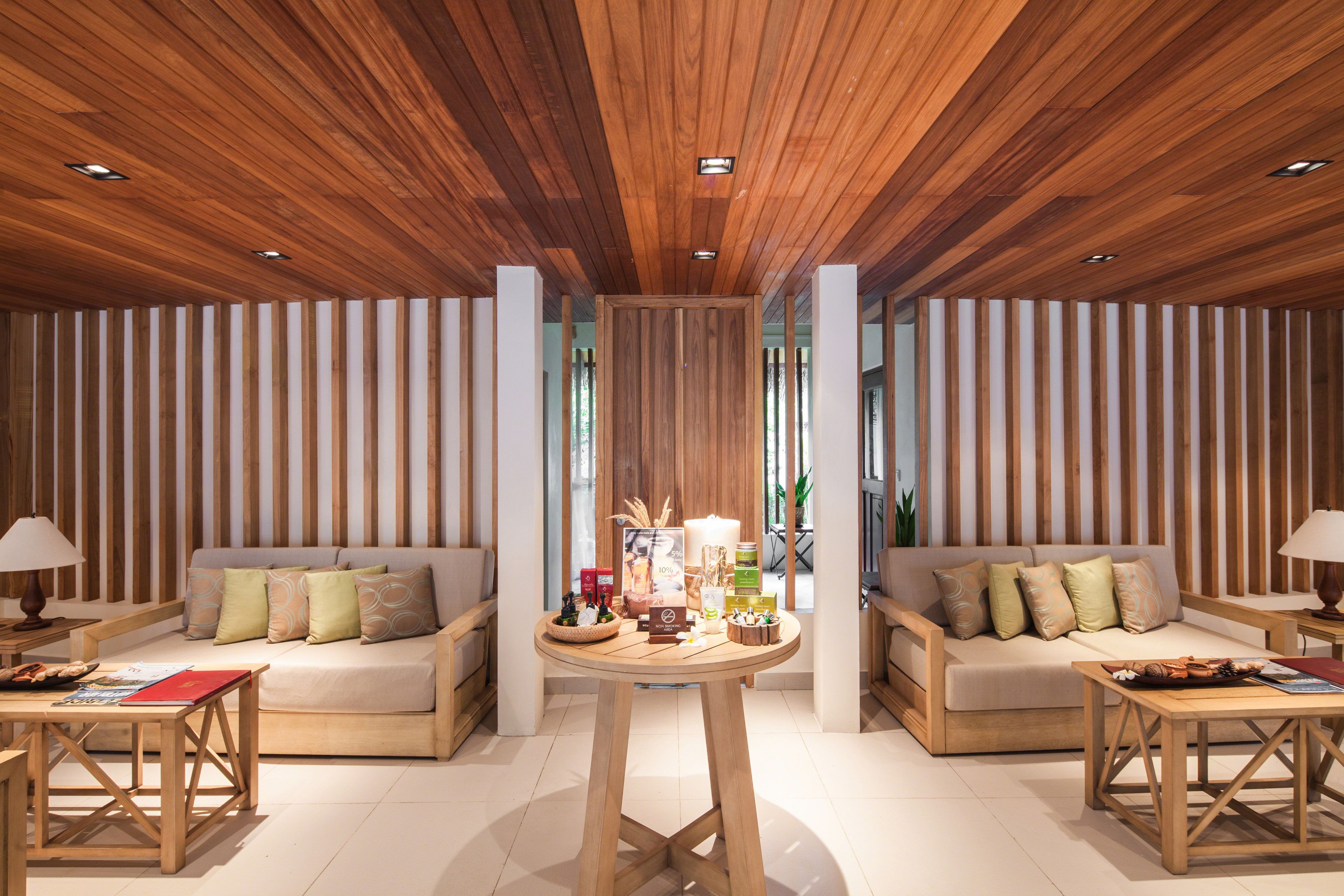 Un interior moderno con techo de madera, dos sofás, una mesa redonda con varios objetos y vistas a la vegetación exterior.
