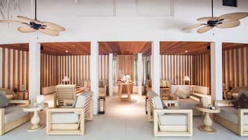 Un área de descanso moderna con muebles de madera, ventiladores de techo y una mesa central.