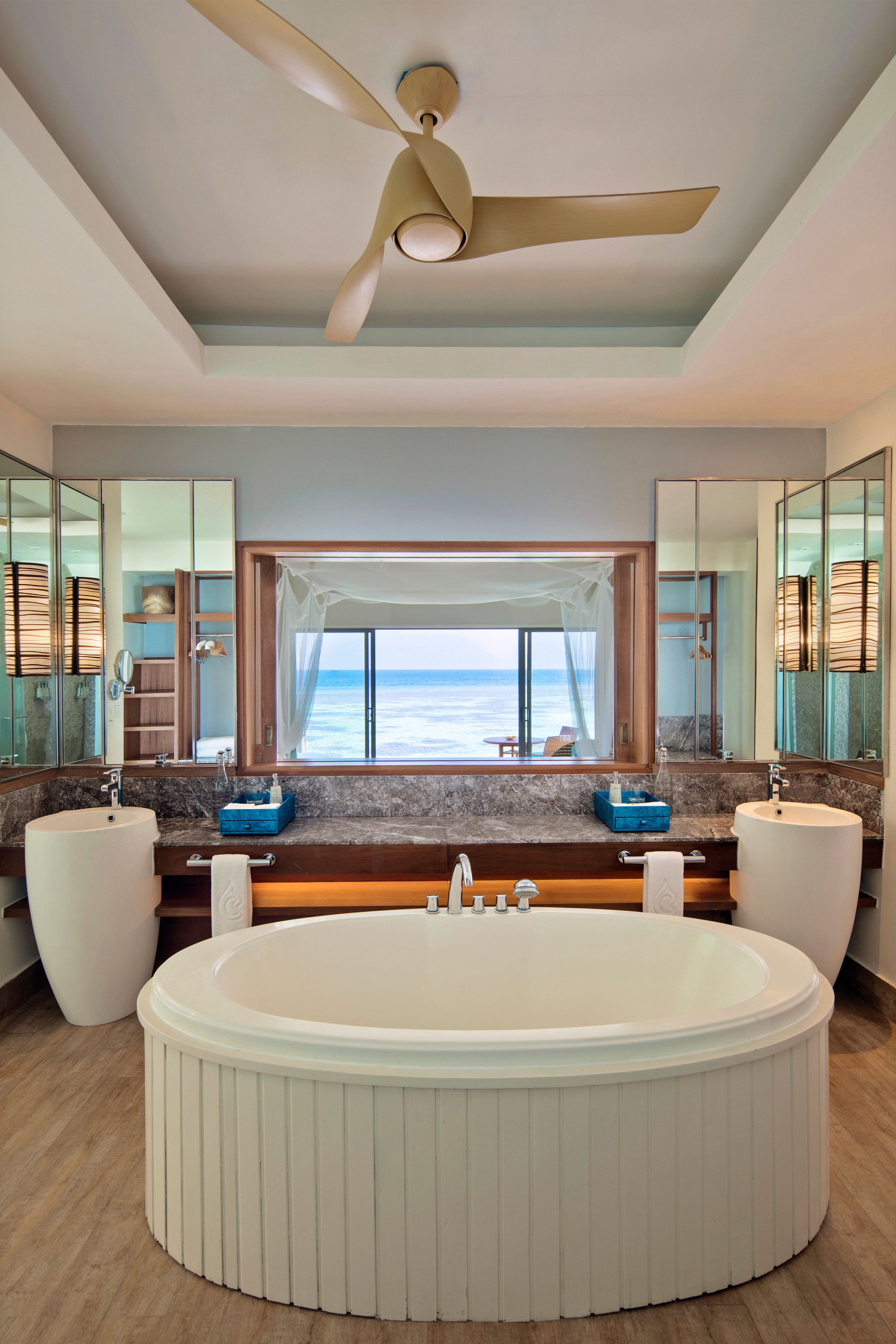 A modern bathroom with a large bathtub, dual sinks, and a view of the ocean.