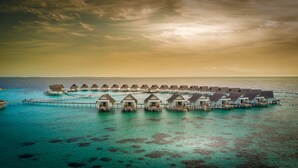 Overwater bungalows connected by walkways, set in turquoise waters with clear skies.