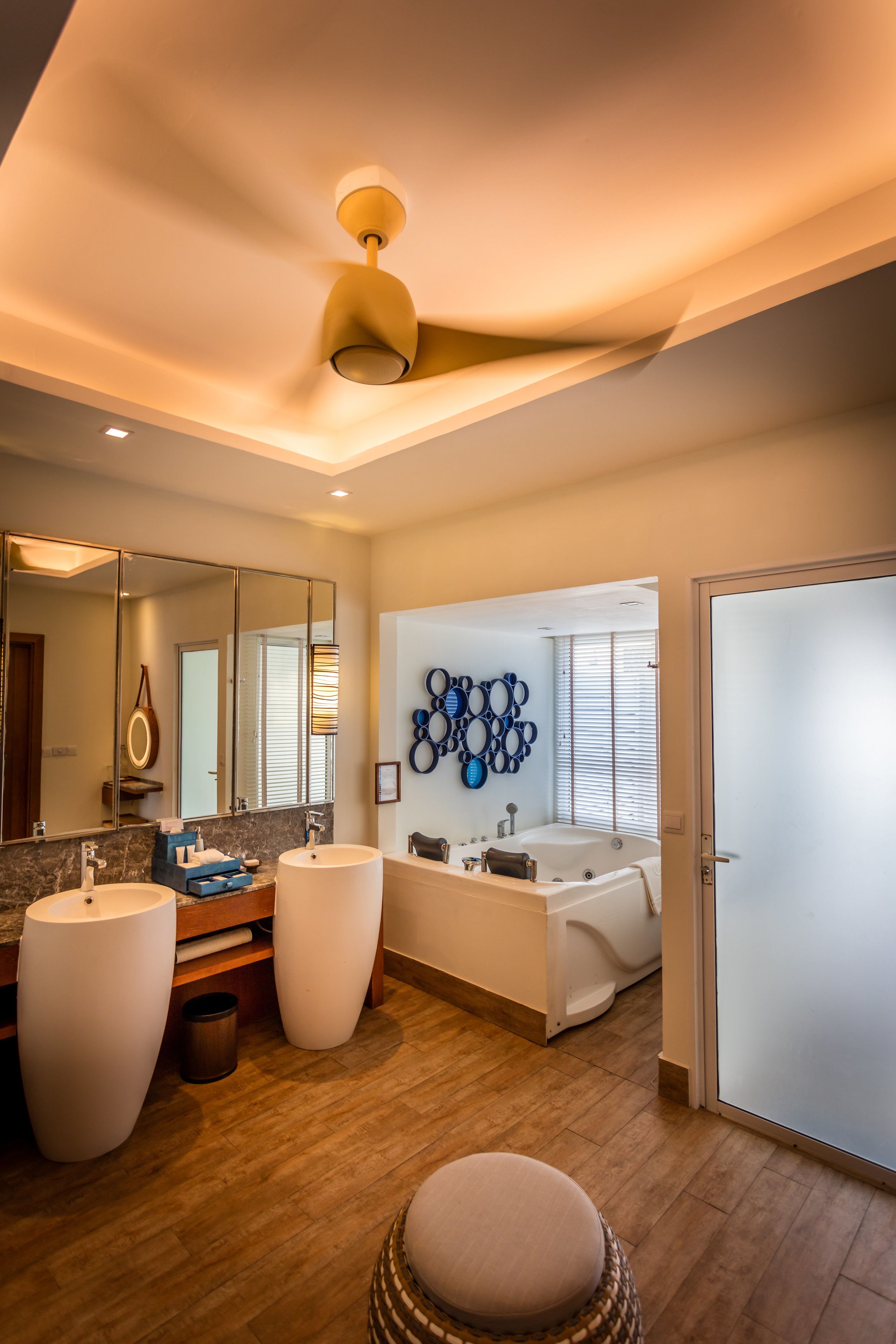 A modern bathroom with a large mirror, two sinks, a bathtub, and a ceiling fan.