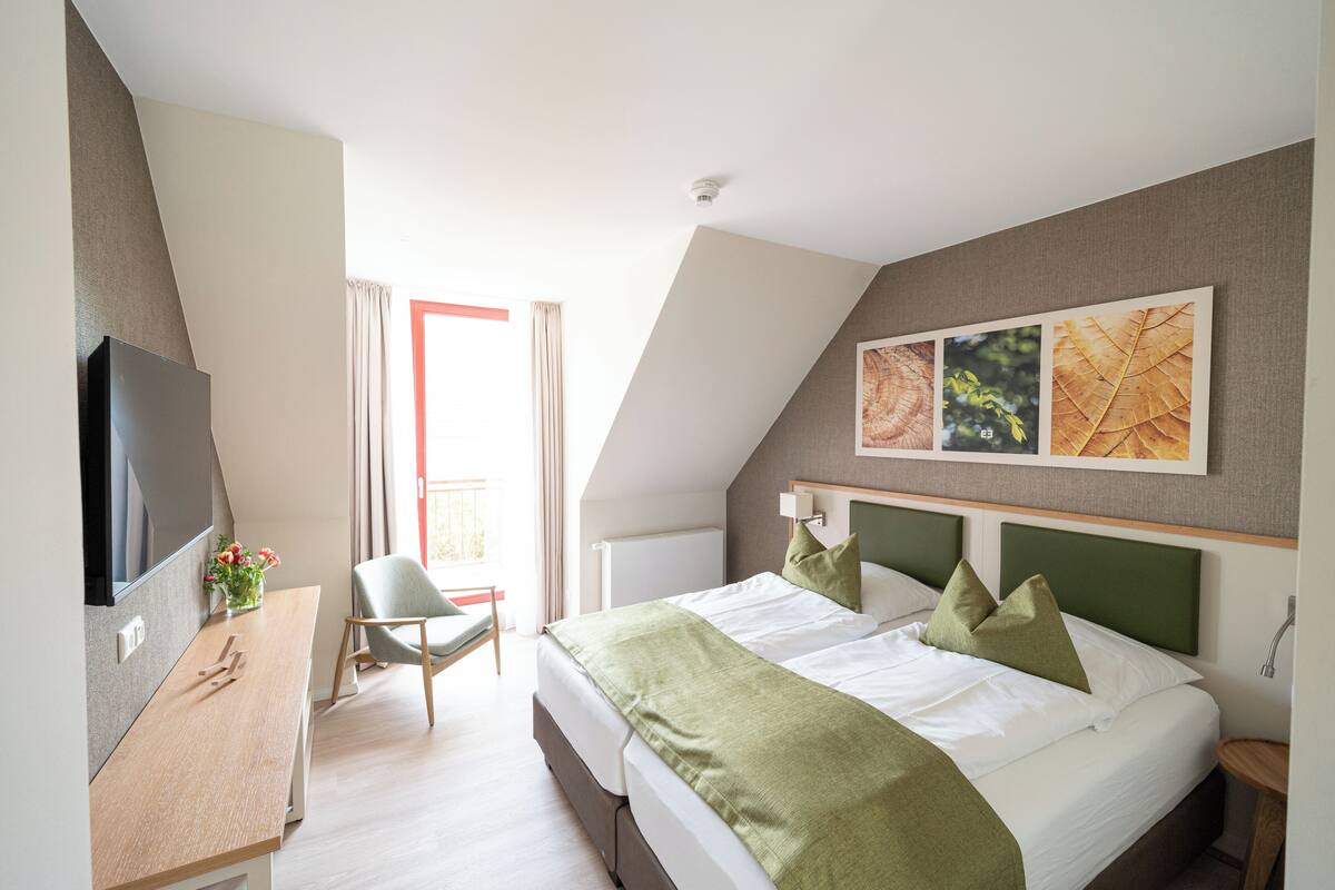 Une chambre d’hôtel avec un lit, un bureau avec une télévision, une chaise et une fenêtre avec des rideaux.
