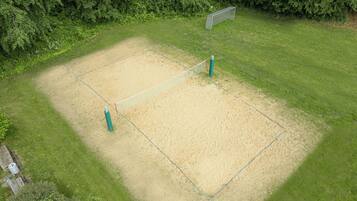 Una cancha de voleibol con red, rodeada de césped y árboles.