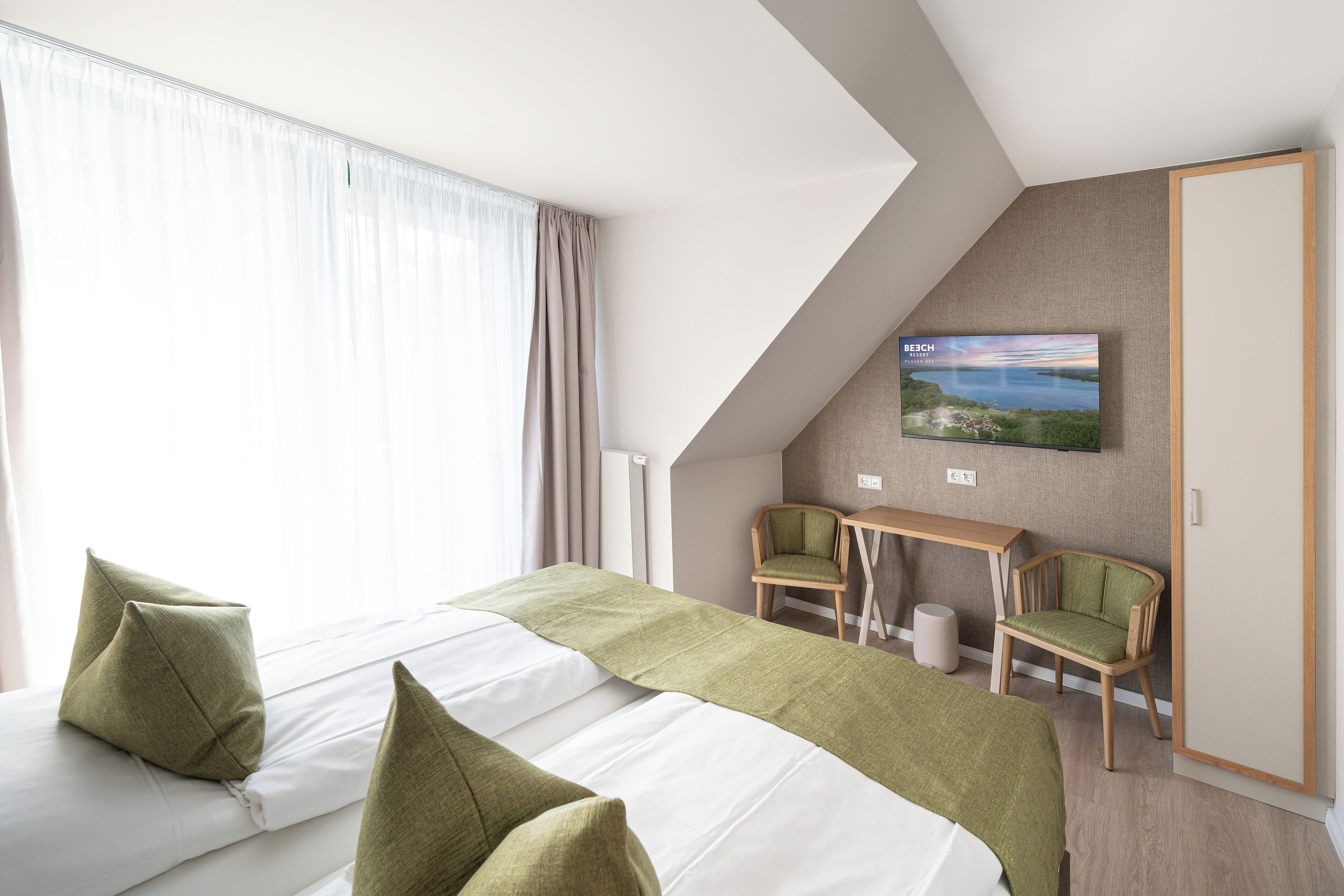 Une chambre d’hôtel avec deux lits, un bureau, deux chaises, une télévision et une vue sur un paysage.