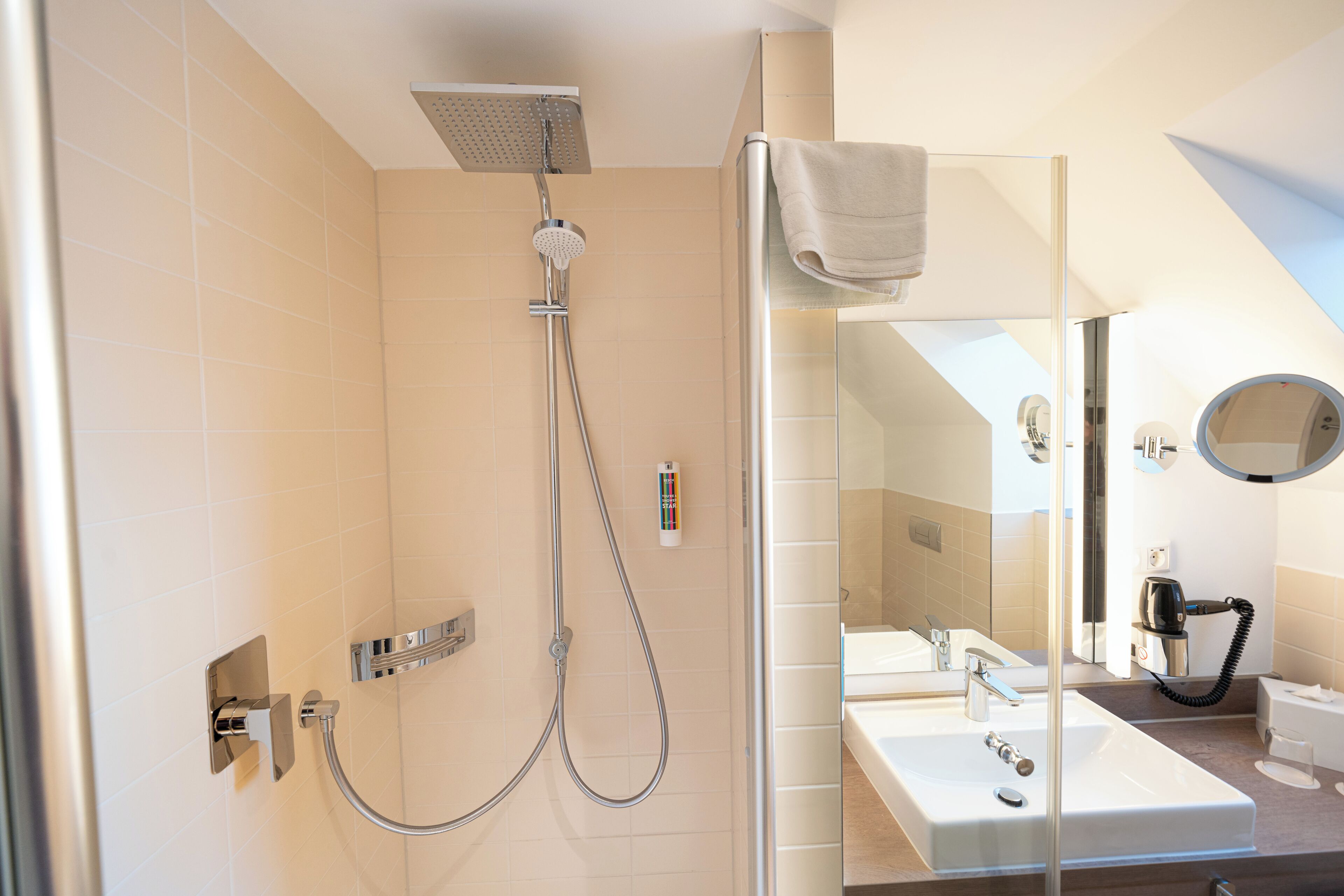 A modern bathroom with a glass shower enclosure, a sink with a mirror, and a towel hanging on the shower door.