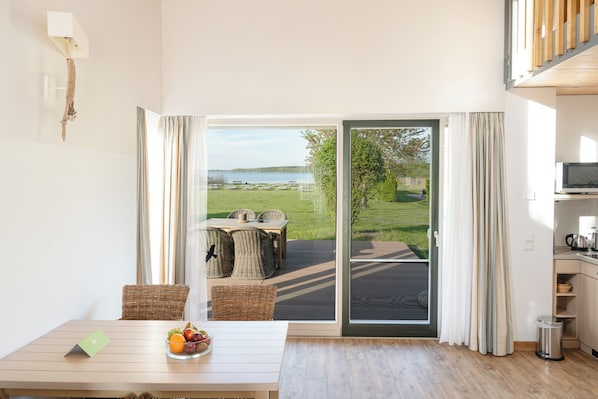 A room with a dining table, wicker chairs, a view of a grassy area and water outside, and a sliding glass door.