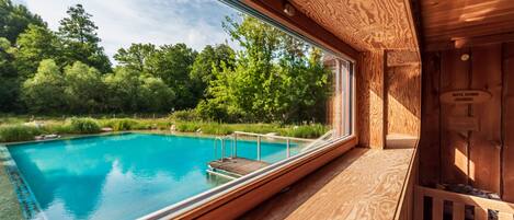 Eine Holzhütte mit einem großen Fenster mit Blick auf einen Swimmingpool, der von üppiger Vegetation umgeben ist.