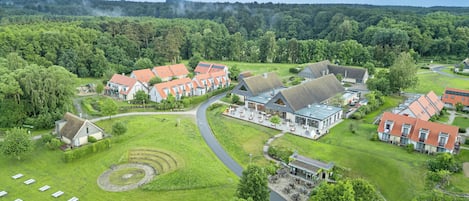 A residential area with multiple houses, a central building with a large patio, and a surrounding green landscape.