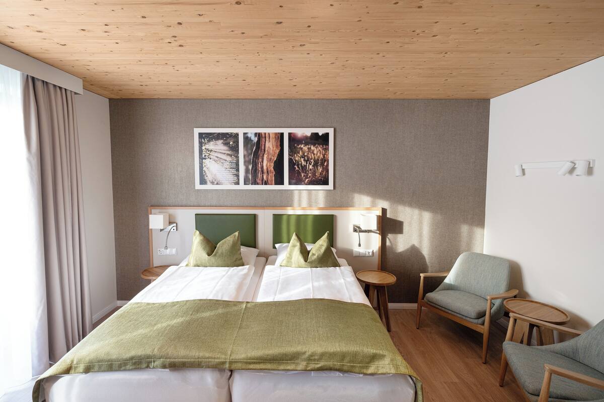 Une chambre d’hôtel avec un plafond en bois, un grand lit avec des oreillers verts, deux tables de chevet, une chaise et une petite table.