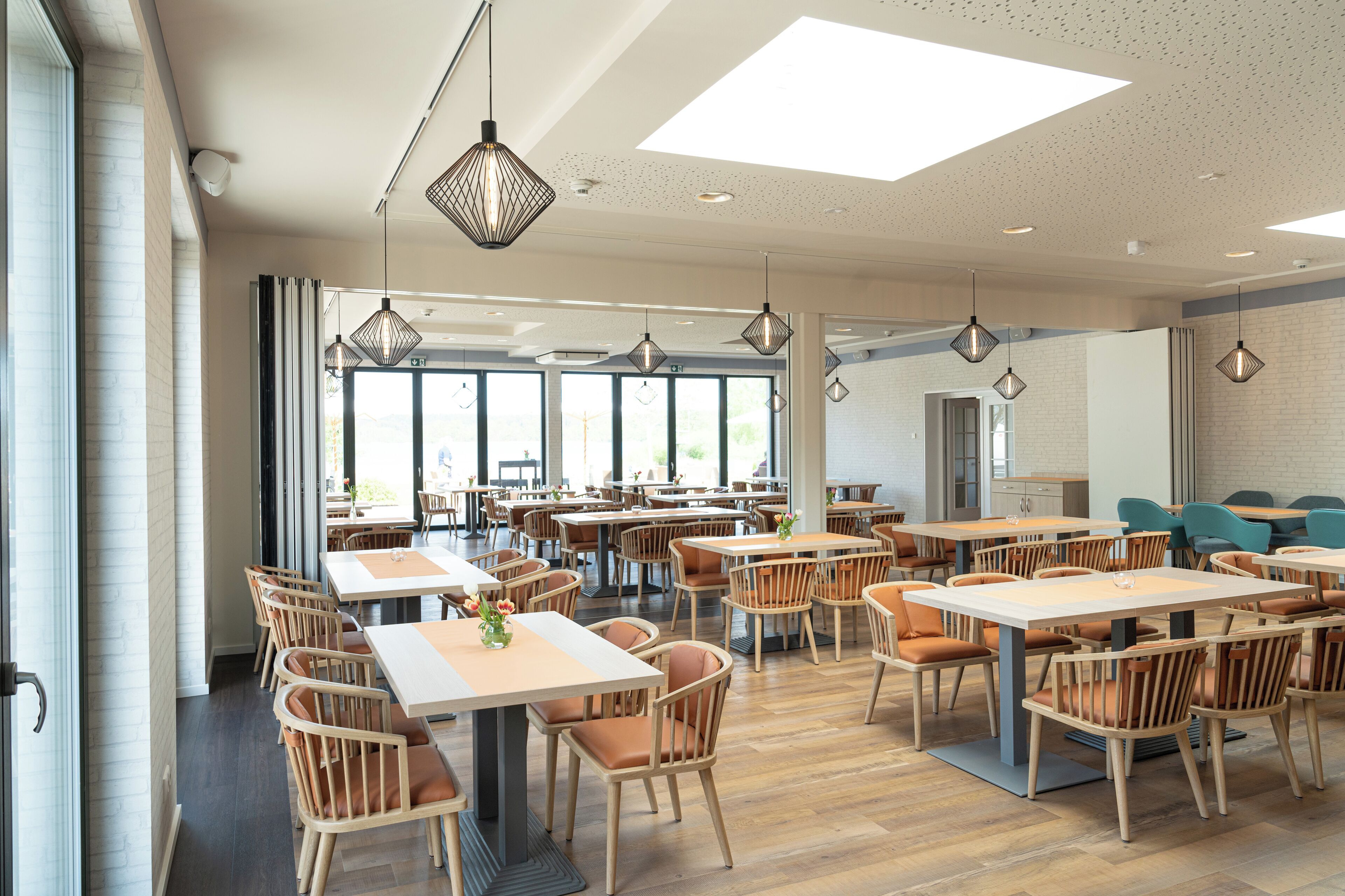 A spacious dining area with multiple tables and chairs, large windows, and pendant lighting.