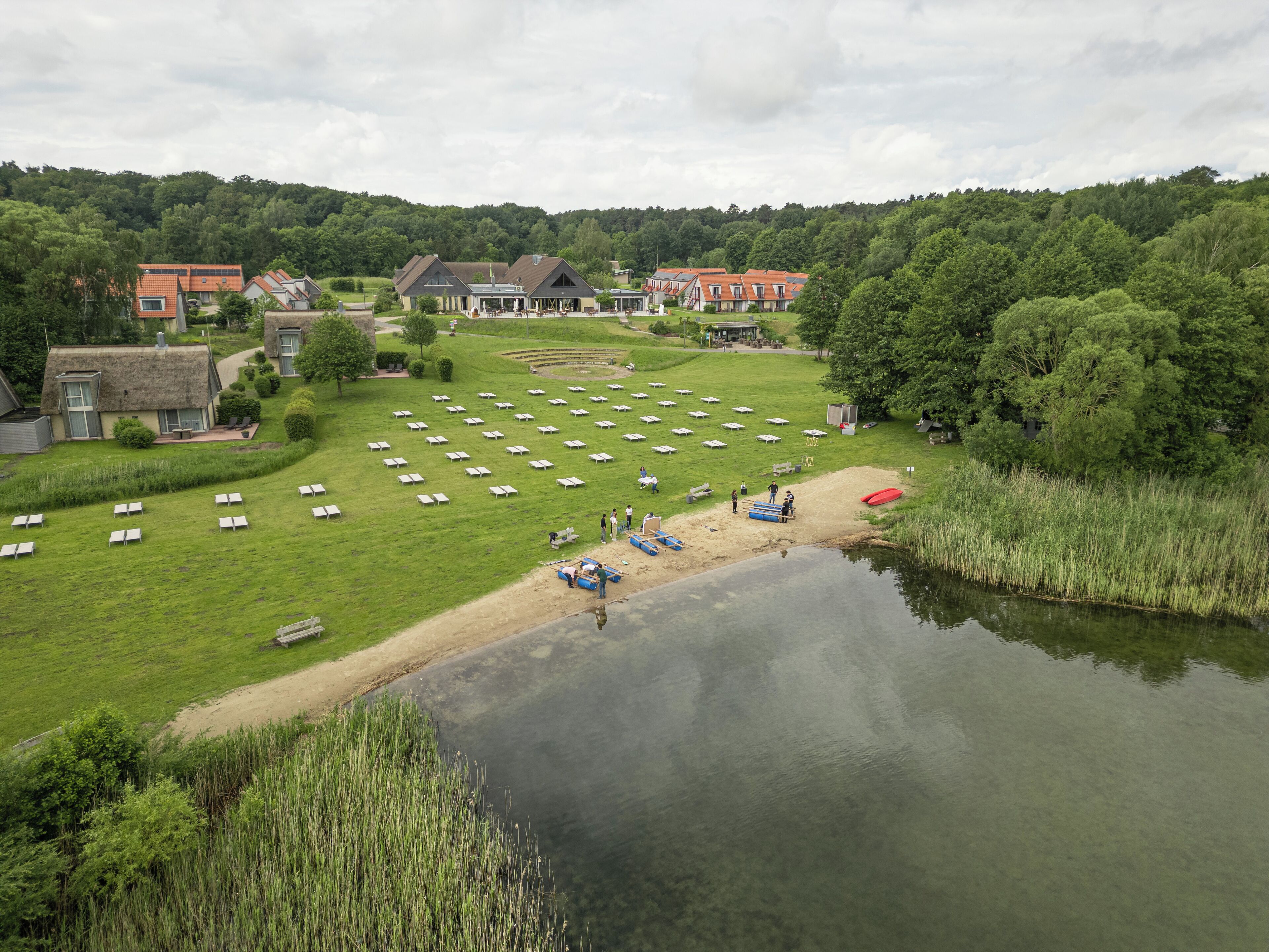 A lakeside property with a grassy lawn, a pond, and a row of houses in the background.