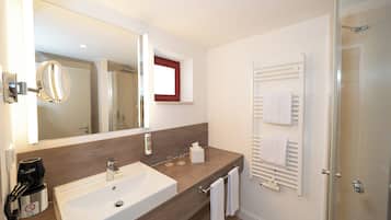 A modern bathroom with a large sink, a mirror, a towel rack, and a glass shower enclosure.