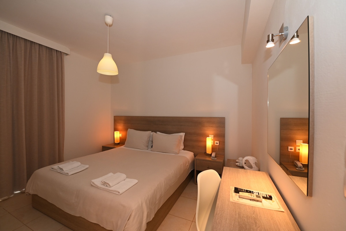 A hotel room with a bed, bedside lamps, a desk with a chair, a mirror, and a telephone.