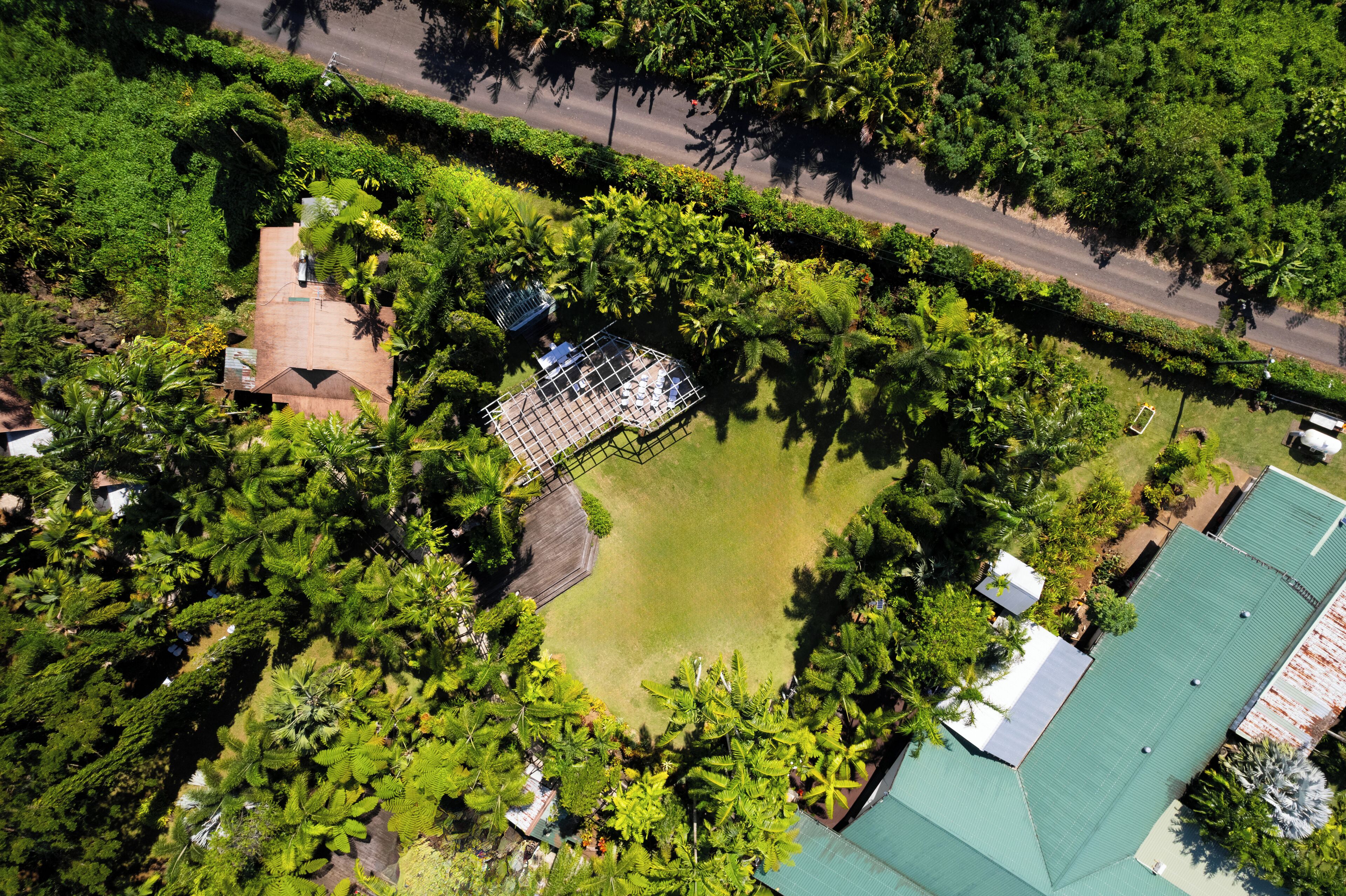 An aerial view of a residential area with a large green lawn, a fenced play area, and a road running alongside.