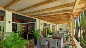 An indoor patio area with wooden beams, wicker furniture, and potted plants. - Orator Hotel Samoa (Apia)