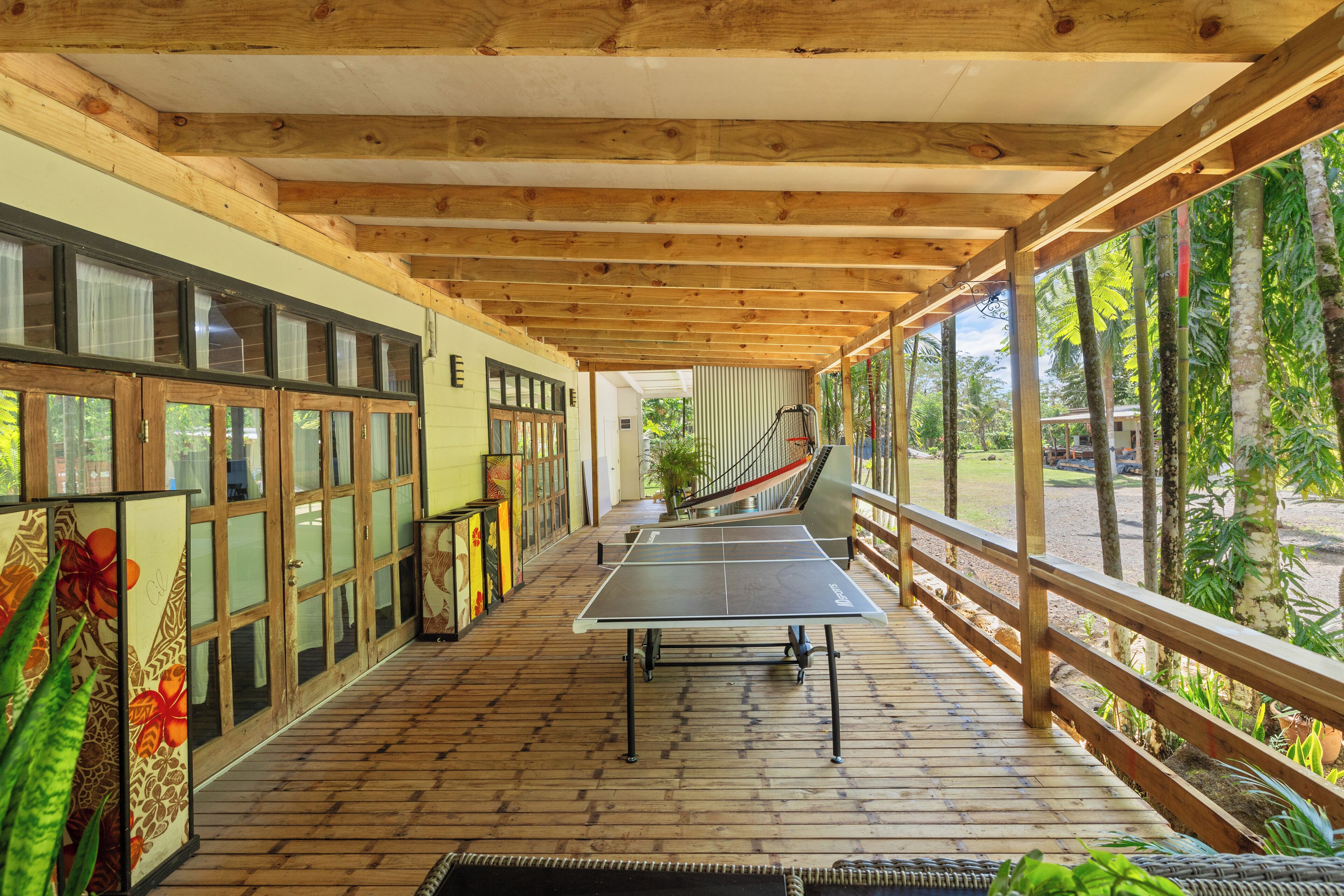 Un espacio al aire libre techado con mesa de ping pong, vigas de madera y vistas al exterior.