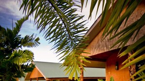 A wooden building with a green roof, surrounded by tropical plants and a wooden pathway. - Orator Hotel Samoa (Apia)