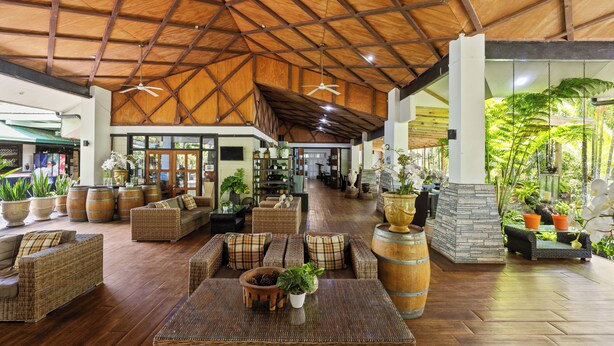 A spacious lobby with high ceilings, wicker furniture, and a variety of potted plants. - Orator Hotel Samoa (Apia)