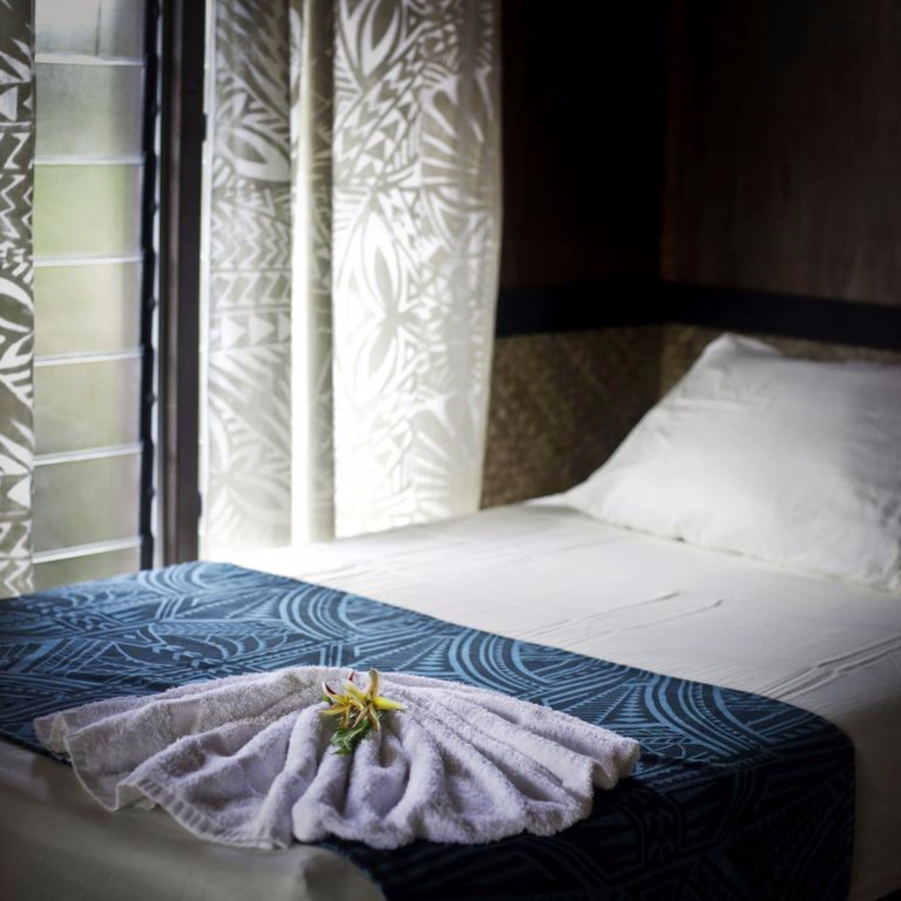 Una habitación de hotel con cama, ventana con cortinas estampadas y toalla con un estampado floral.
