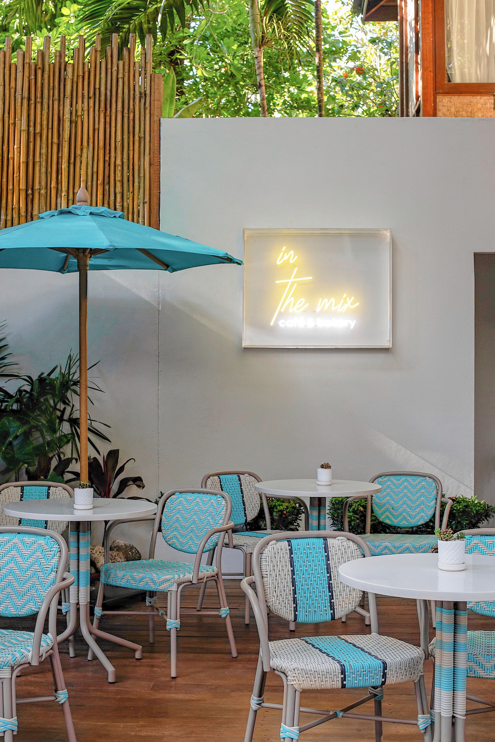 An outdoor seating area with wicker chairs and a neon sign.