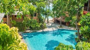 A clear blue pool surrounded by lush greenery and a beach path leading to a building with a thatched roof. - Buri Rasa Village Phangan (Ko Pha-ngan)