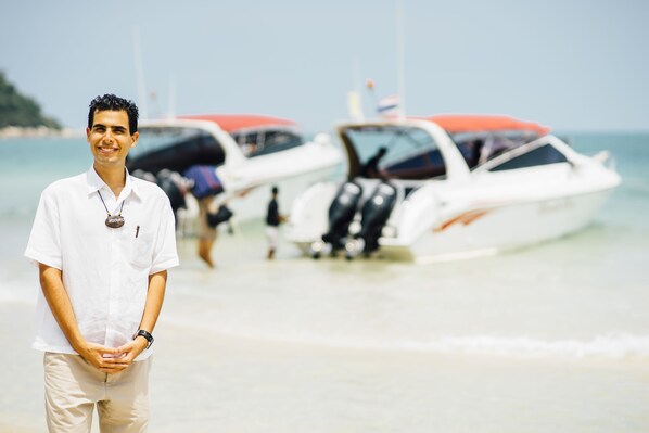 A man standing in front of a beach with boats in the background.