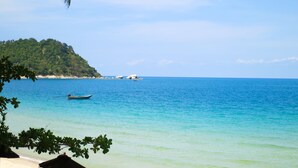 A beach with clear turquoise water, a boat, and a lush green hill in the background. - Buri Rasa Village Phangan (Ko Pha-ngan)