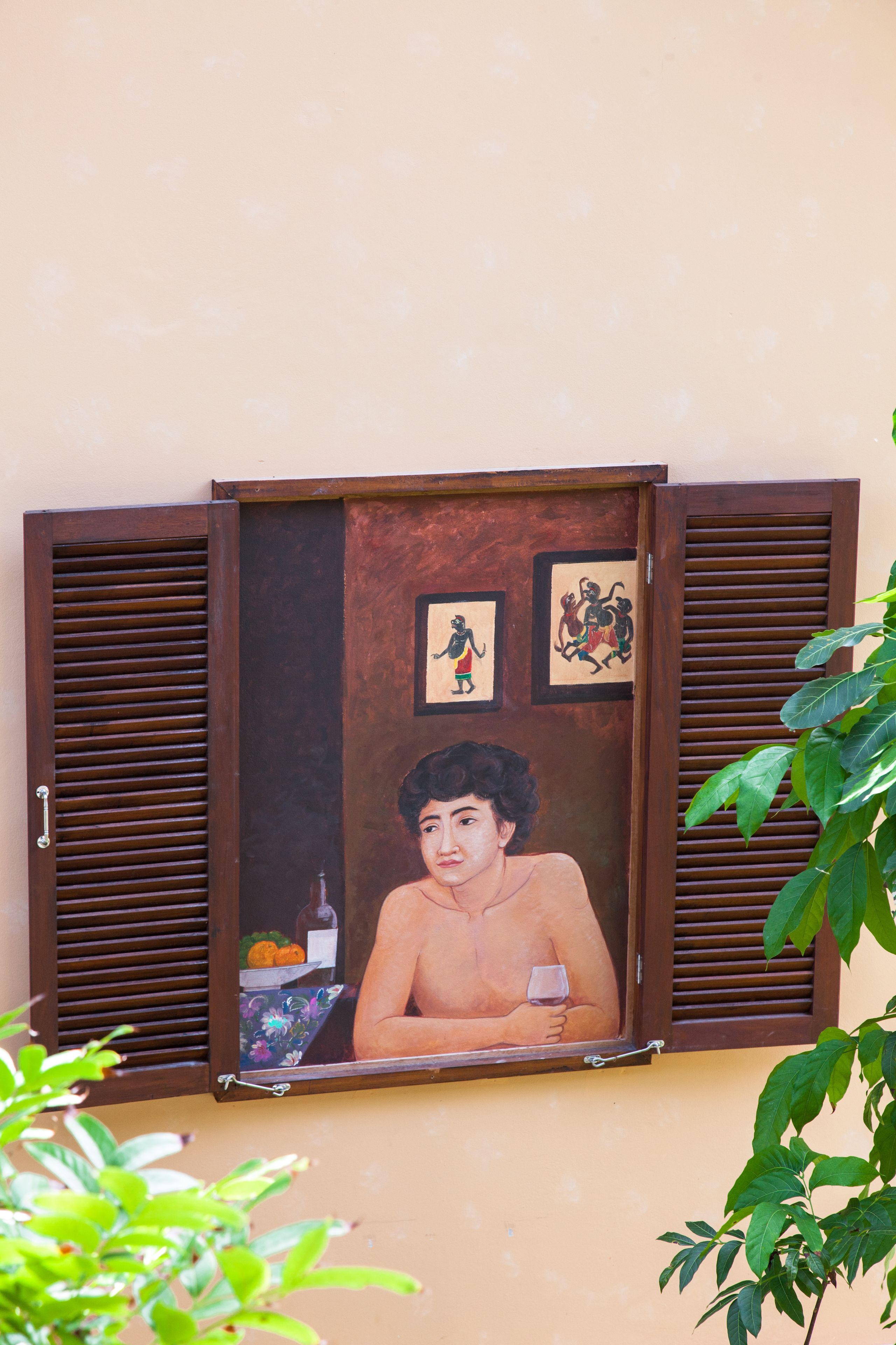 Una puerta de madera con un ventanal de vidrio, un cuadro con la imagen de una persona sosteniendo un vaso, y dos cuadros más pequeños arriba.