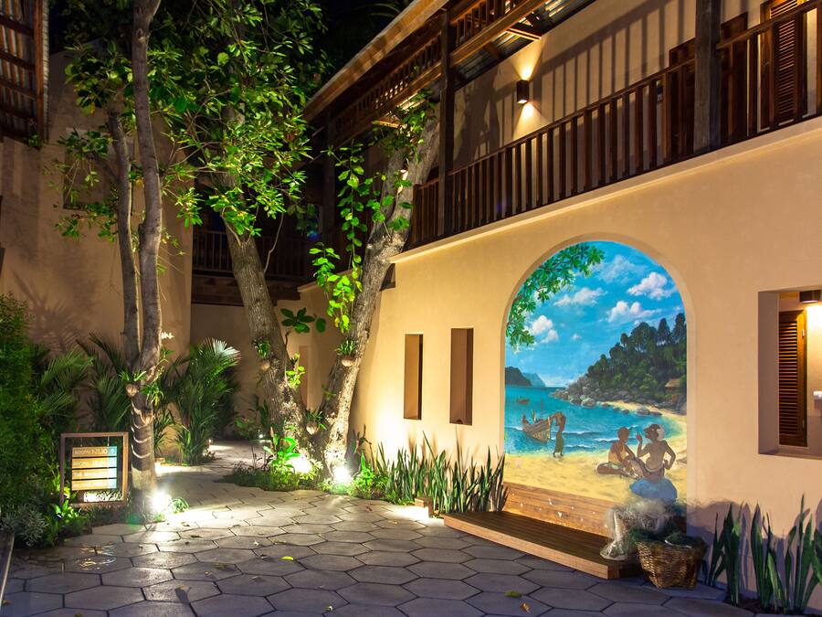 A hotel courtyard with a mural of a beach scene, a wooden deck, and a stone pathway.