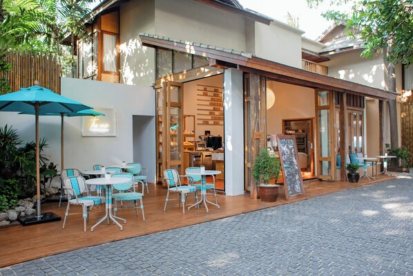 An outdoor seating area with tables and chairs, a wooden fence, and a building entrance. - Buri Rasa Village Phangan (Ko Pha-ngan)