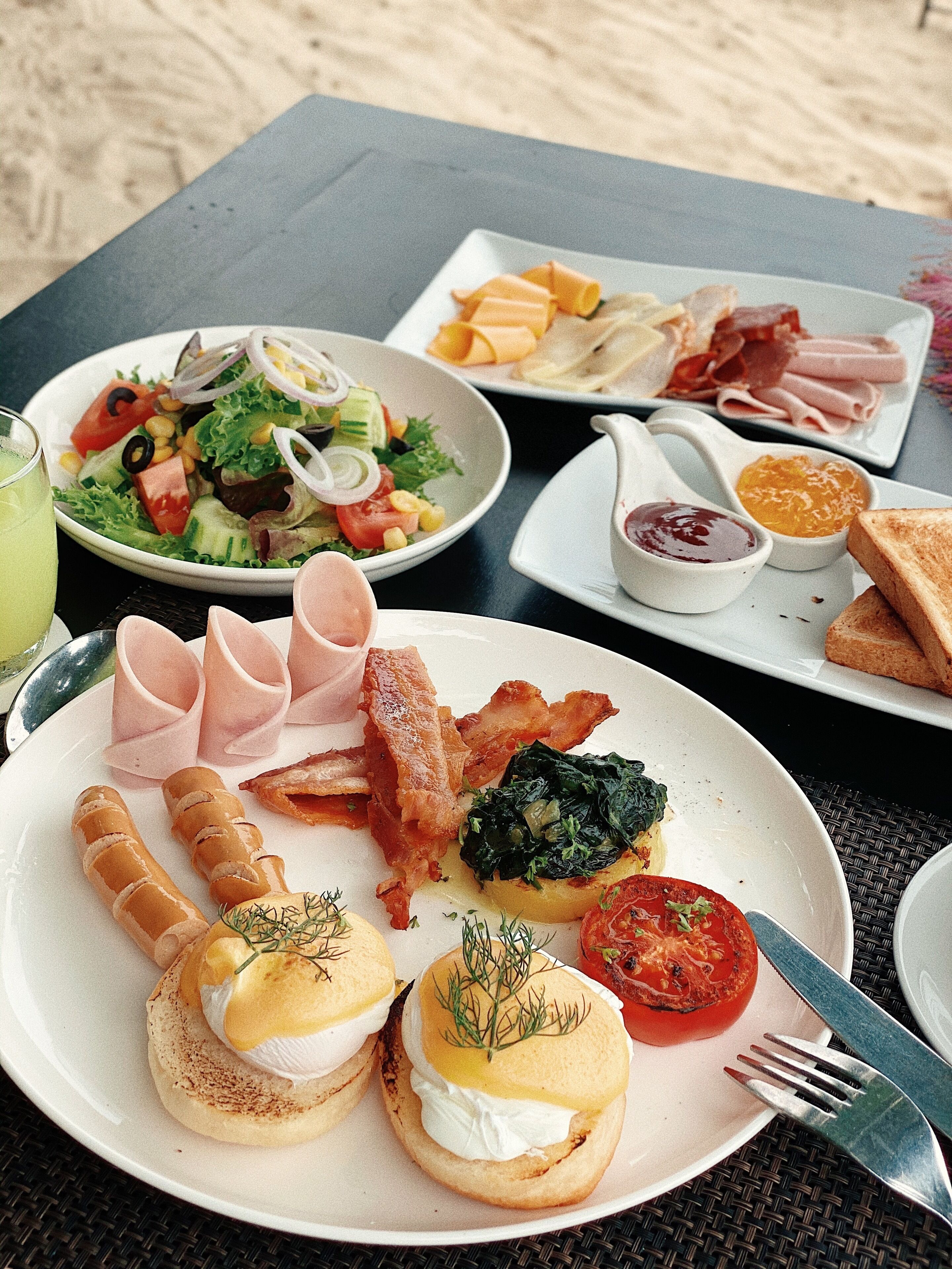 A breakfast spread on a table with various dishes including eggs, bacon, toast, and a salad.