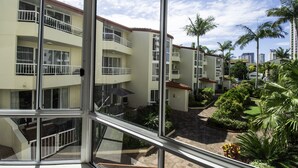 A multi-story residential building with balconies, a courtyard with palm trees, and a view of the surrounding urban area. - Key Largo Apartments (Burleigh Heads)