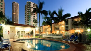 A pool area with lounge chairs, a brick pool, and tall buildings in the background. - Key Largo Apartments (Burleigh Heads)