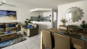 A modern living room with a sofa, coffee table, and dining area. - Key Largo Apartments (Burleigh Heads)