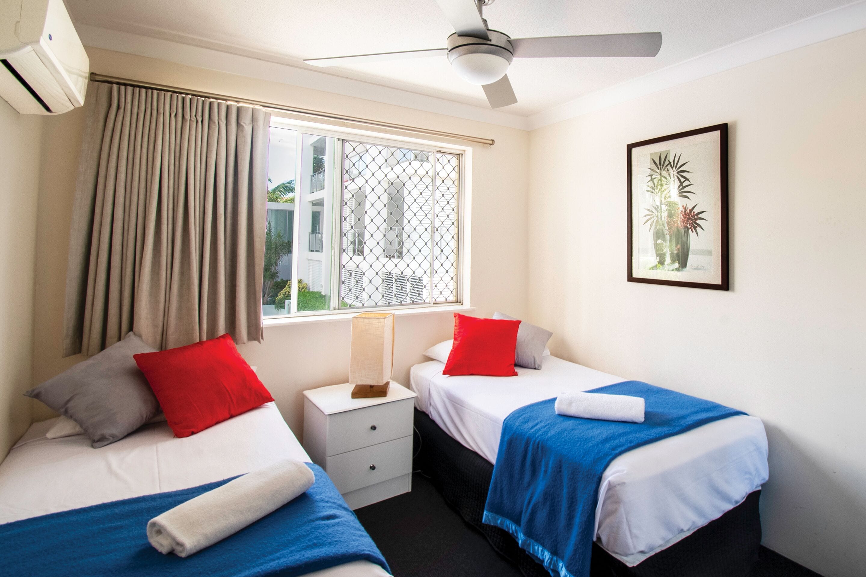 A hotel room with two beds, a window with a view, a ceiling fan, and a framed picture on the wall.