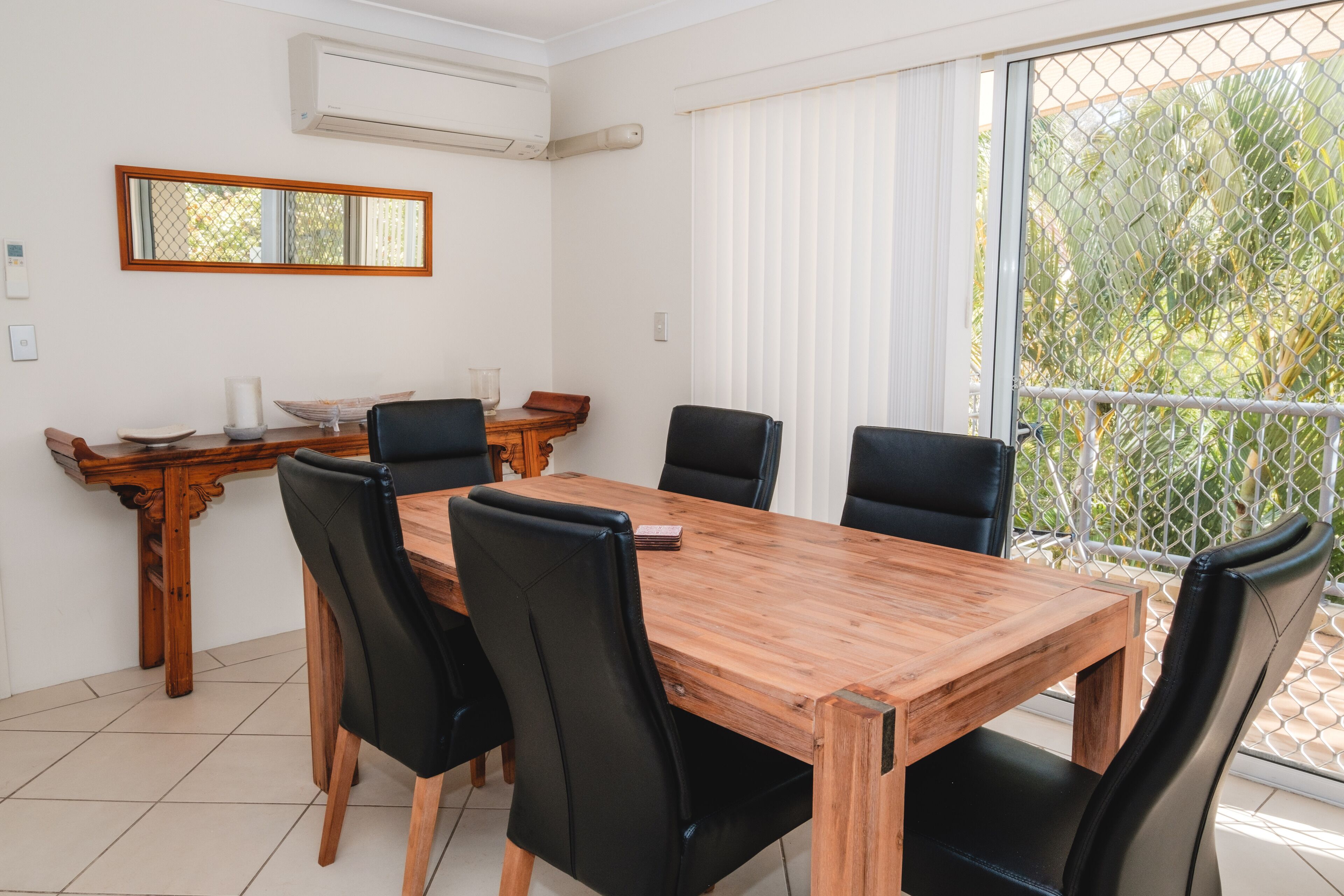 A dining area with a wooden table and black chairs, a wooden side table, and a window with blinds.