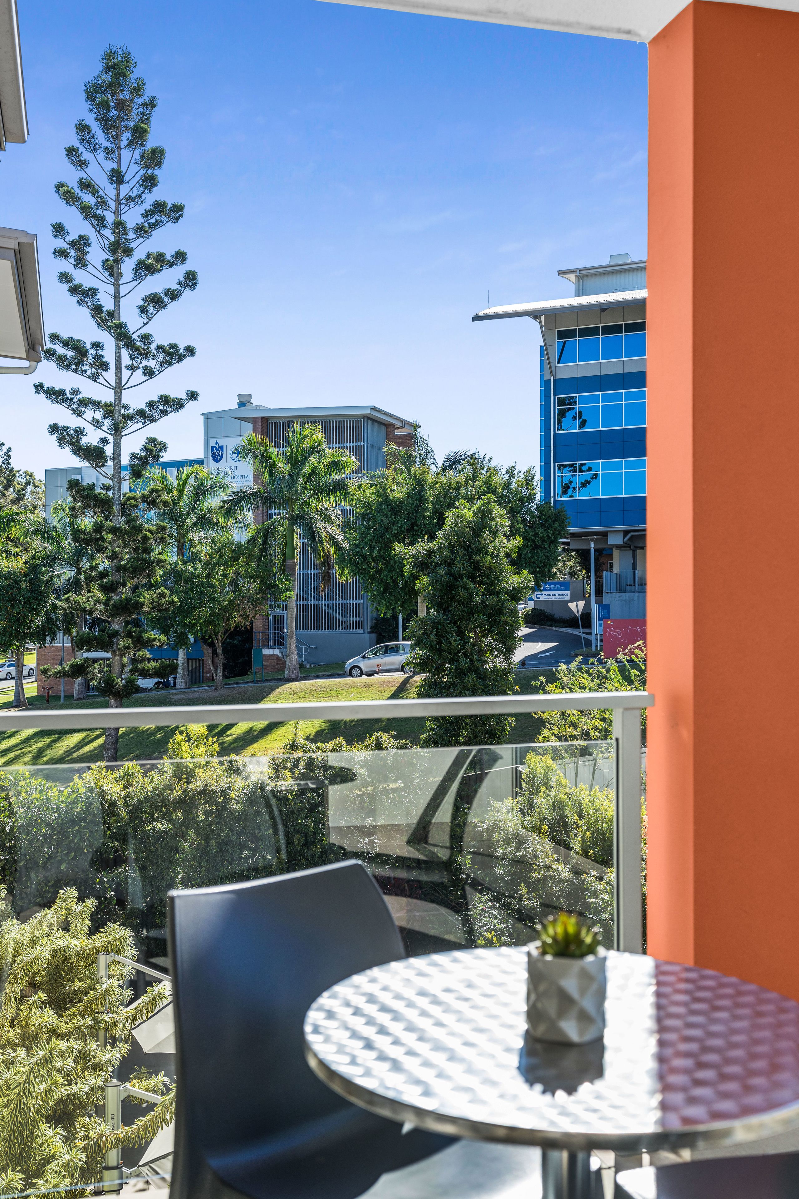 Un balcon avec une table et des chaises, donnant sur un immeuble à la façade bleue et bordé de palmiers.
